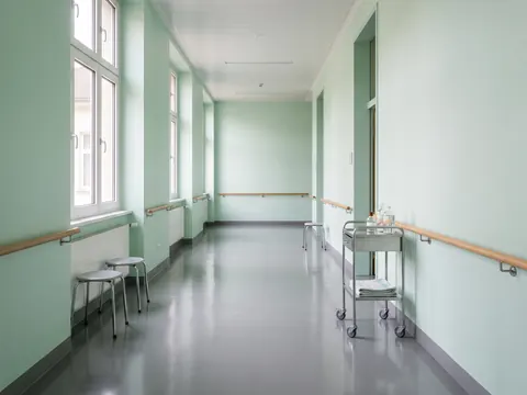 Szpitalny korytarz ze zmywalnymi ścianami w jasnomiętowym kolorze i szarą posadzką przemysłową